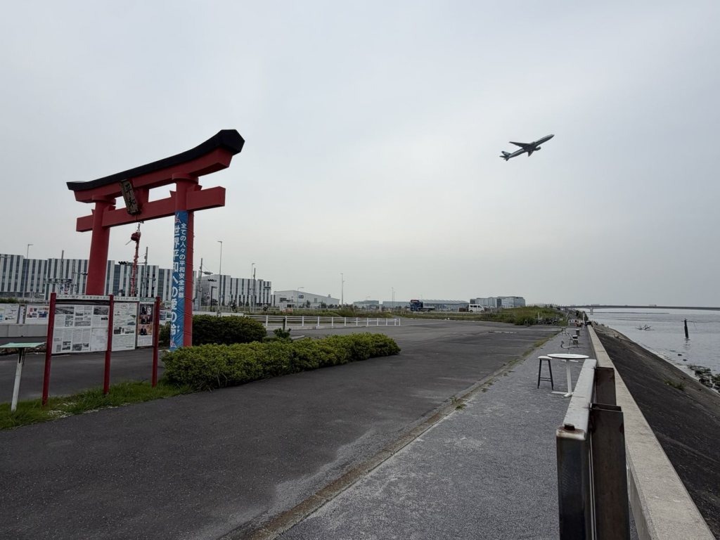 A large red torii gate near Haneda Airport with a passenger jet taking off overhead
