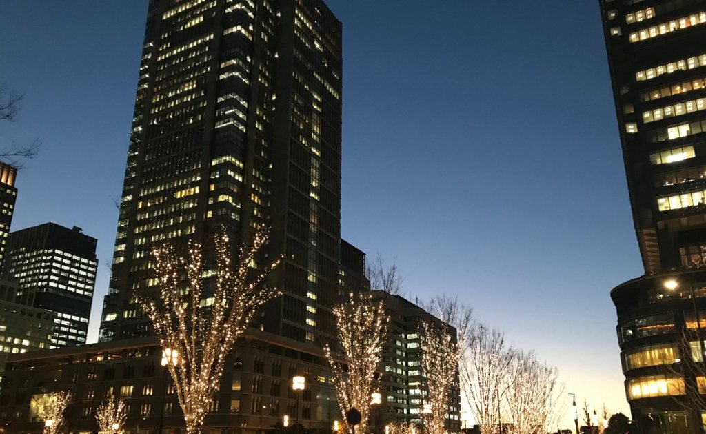 Street trees covered in warm white lights in front of office towers in Marunouchi at dusk