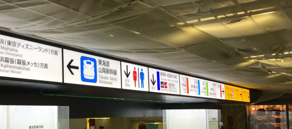 Bilingual color-coded signs inside Tokyo Station pointing to the Tokaido Shinkansen, Narita Express, and JR lines